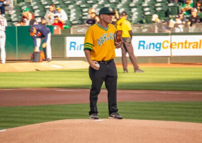 Baseball coach Chris Kyriacou throws the ceremonial first pitch at the Oakland Coliseum
