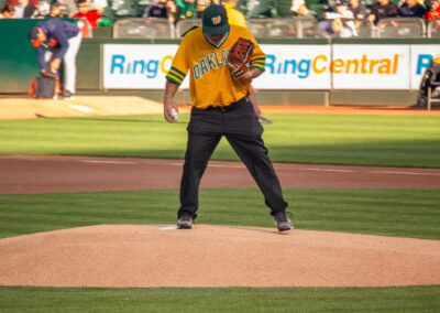Baseball coach Chris Kyriacou throws the ceremonial first pitch at the Oakland Coliseum
